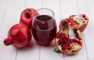 side view glass of pomegranate juice with pomegranates on white background